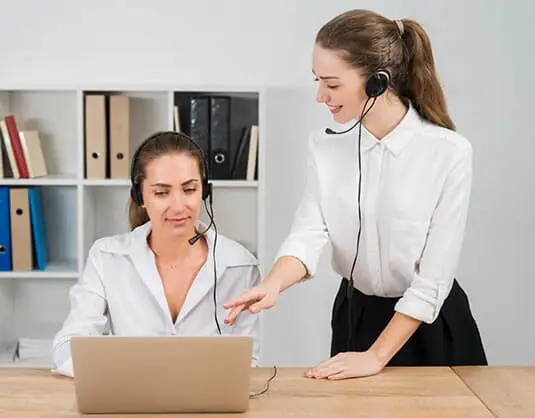 One Girl Working On Laptop & Other Girl Explaining Her