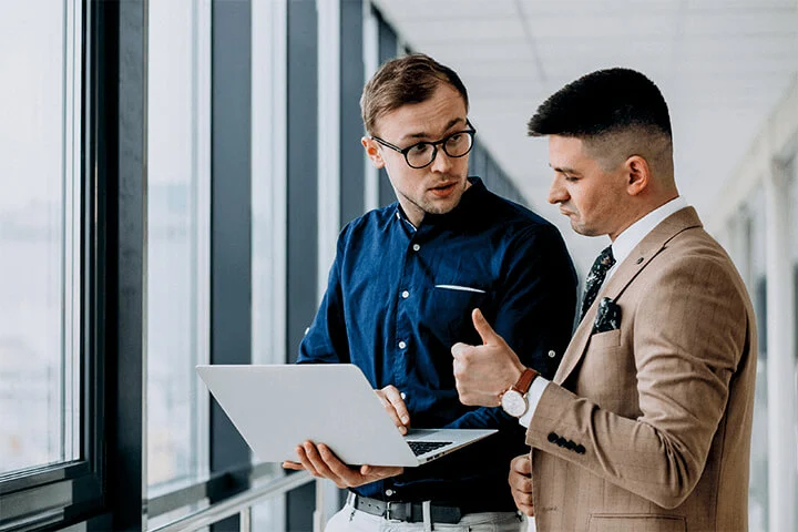 Two Men's Discussing From Them One Looks At Laptop Showing Thumbs Up Symbol